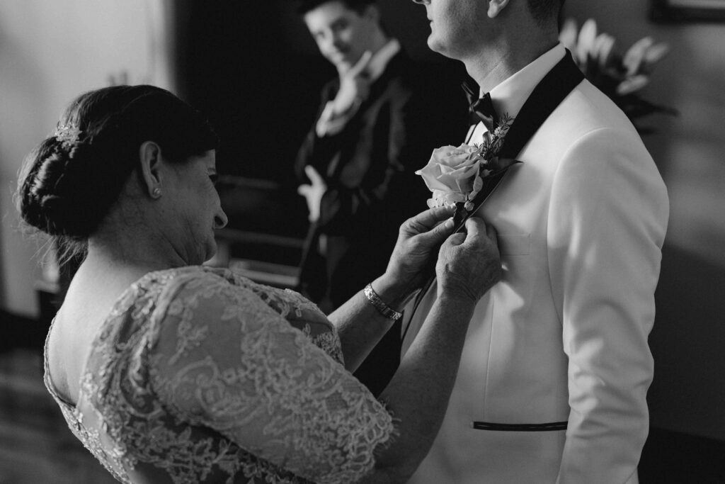 Mother of the groom pinning on his floral buttonhole.